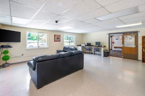 A black couch sits in the middle of a spacious room with a television and a window.