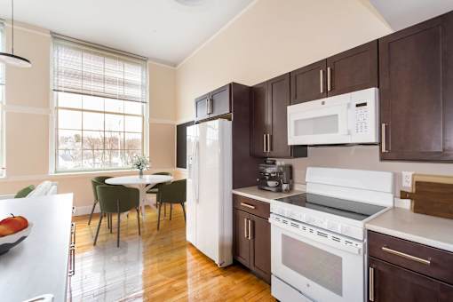 a kitchen with brown cabinets and white appliances and a table with chairs at Beverly Village for Living & the Arts Apartments, Massachusetts