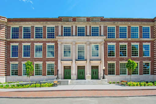 a large brick building with green doors and white columns at Beverly Village for Living & the Arts Apartments, Beverly, 01915