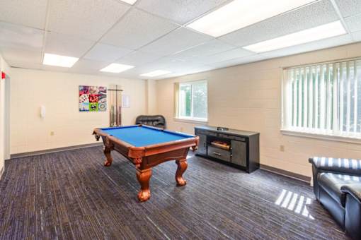 A pool table in a room with a black leather couch and a TV.