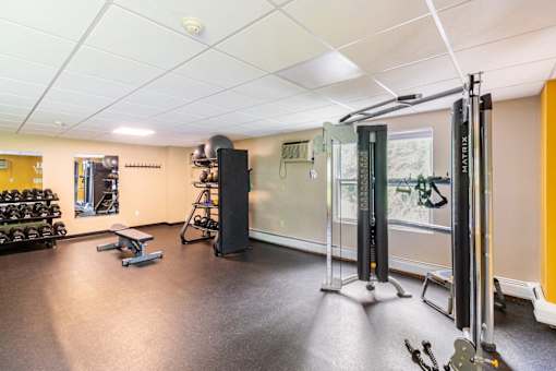 A gym with a weightlifting area and a bench. at Ship's Watch Apartments, Fall River, MA, 02720