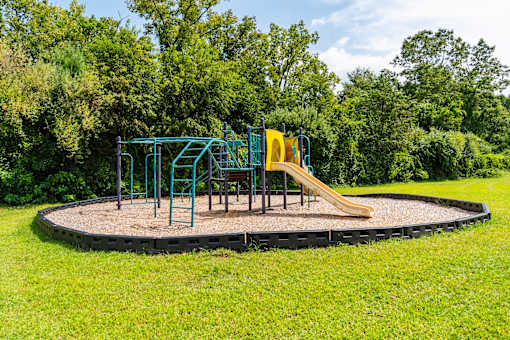 A playground with a slide and swings set in a grassy area at Coppermine Village Apartment , Connecticut, 06010