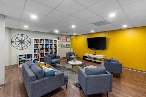 A living room with a grey sofa, a grey armchair, a coffee table, a bookshelf, and a TV. at Ship's Watch Apartments, Fall River, MA, 02720