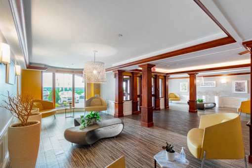 A modern living room with a yellow chair and a large window. at Ship's Watch Apartments, Fall River, MA, 02720