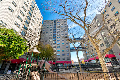 A playground with a slide and a tree in front of apartment buildings.