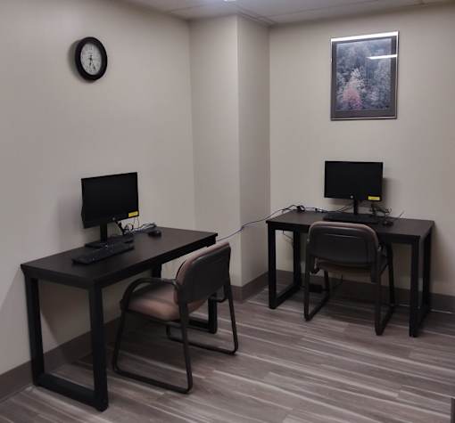 Two black computer desks with chairs and a clock on the wall.
