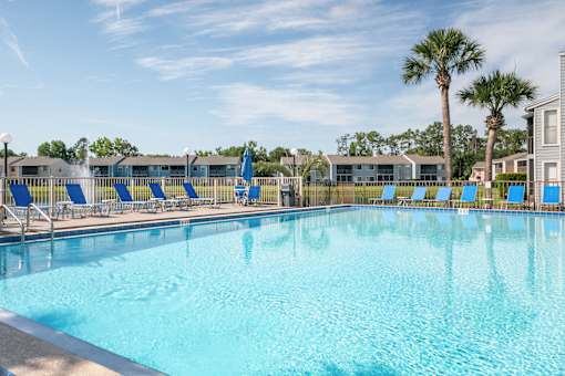 A large swimming pool with blue water and lounge chairs Fishermans Landing Apartments in Ormond Beach, FL.