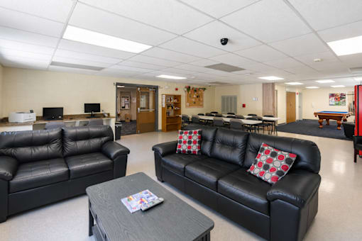 A black leather couch with a red and white pillow sits in a room with a wooden coffee table in front of it.