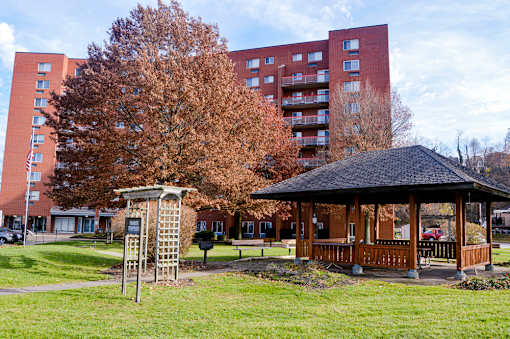 A gazebo sits in a grassy area in front of a red brick building.