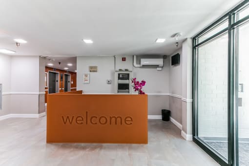 a large orange welcome sign sits in front of a white wall with glass doors