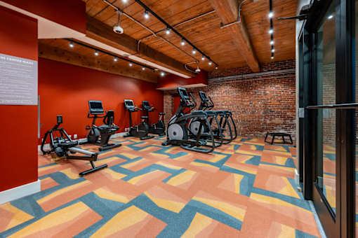 A gym with a variety of exercise equipment and a colorful floor at The Cordovan at Haverhill Station, Haverhill, MA