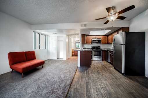 A red couch sits in a spacious kitchen and living room with wood flooring and modern appliances.