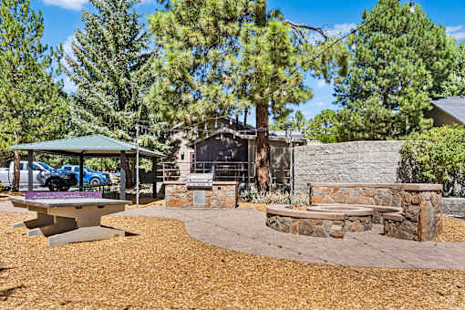 A backyard with a picnic table, a fire pit, and a stone wall.