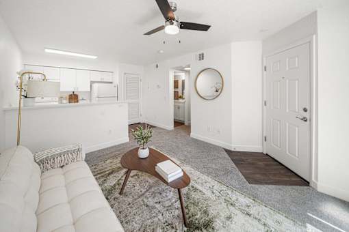 A white living room with a couch, coffee table, and a ceiling fan.