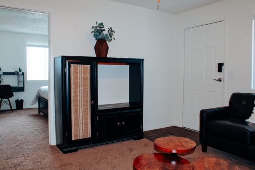 a living room with a black chair and a black china cabinet with a plant on top