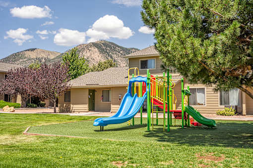 A playground with a blue slide and a red slide in front of a house.