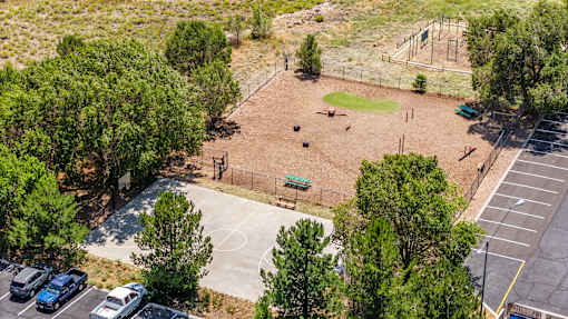 A park with a basketball court, dog park, and a parking lot.