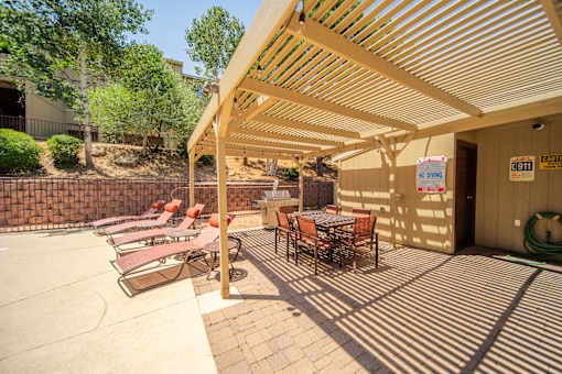 A patio with a table and chairs under a wooden roof.