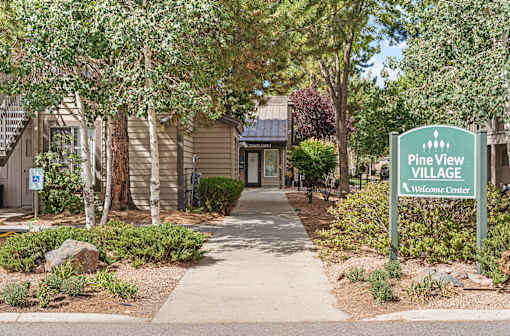 A sign that says Pine View Village Welcome Center stands in front of a building.