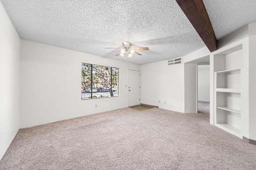 A room with a ceiling fan and a window with a view of trees.