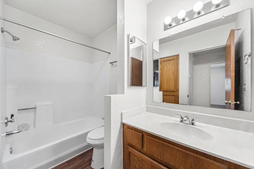 A white bathroom with a wooden vanity and a white bathtub.