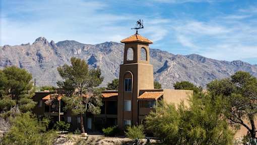 Altamira tower with weather vane on top is surrounded by trees and mountains.