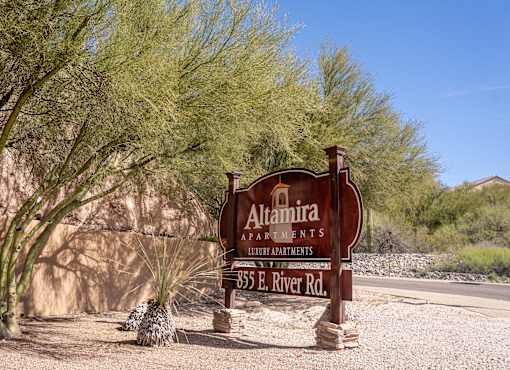 A sign for Altamira Apartments stands in front of a tree.