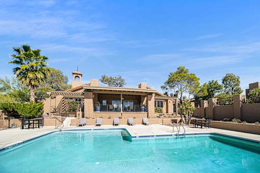 A swimming pool in front of a house with a patio and trees.