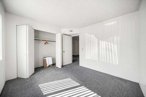 A bedroom with white walls and grey flooring and closet.