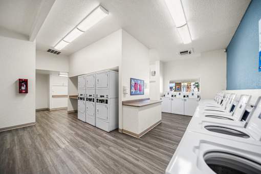 A laundry room with washers and dryers lined up on both sides of the room.