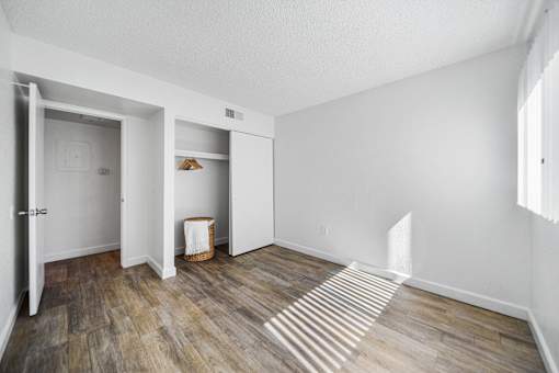 A room with white walls and wooden flooring with a doorway open to another room.