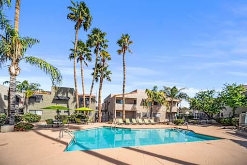 A swimming pool surrounded by palm trees and a building in the background.