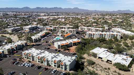 A large apartment complex is surrounded by a parking lot and other buildings.