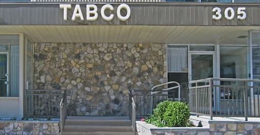 The front of a building with a stone wall and a sign that says "TABCO 305".