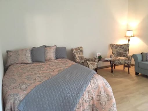 A bed with a blue comforter and matching pillow cases sits in a room with a chair and a small table.