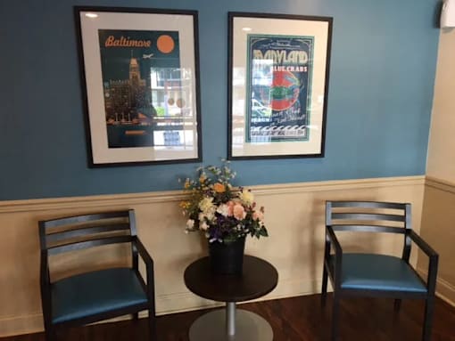 Two framed posters on a wall above a table with two chairs and a vase of flowers.