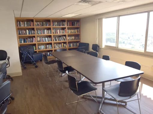 A room with a long table, chairs, and a bookshelf filled with books.