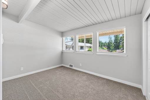 A room with a carpeted floor and a window showing a view of trees and a house.