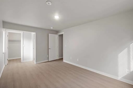 A room with white walls and wooden flooring with two open doors.