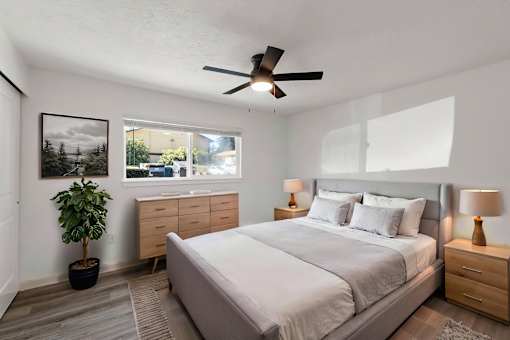 A bedroom with a large bed, a ceiling fan, and a potted plant.