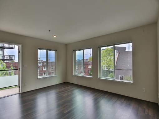 Empty living room with a wood floor and three windows  at Charbonneau Apartments in Seattle, WA 98101