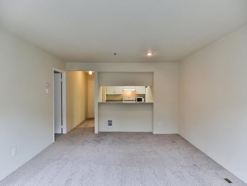Empty living room with a kitchen in the distance  at Charbonneau Apartments in Seattle, WA 98101
