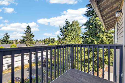 A balcony with a metal railing overlooks a parking lot and trees.