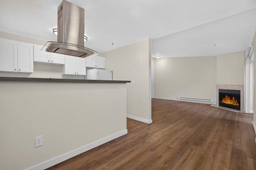 A modern kitchen with a stainless steel range hood and a fireplace in the living room.