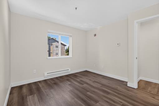 A bedroom with wood plank flooring and a window with heating at Ridgeline Apartments