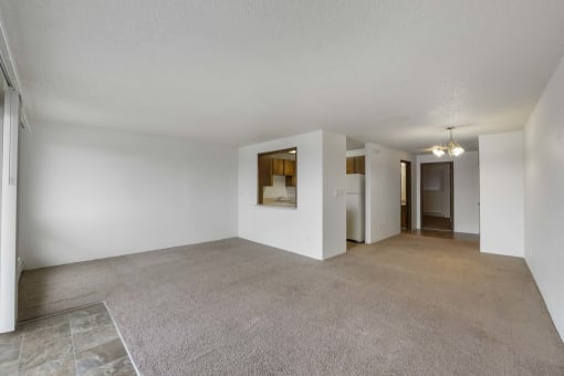 the living room and dining room of an apartment with white walls and carpet