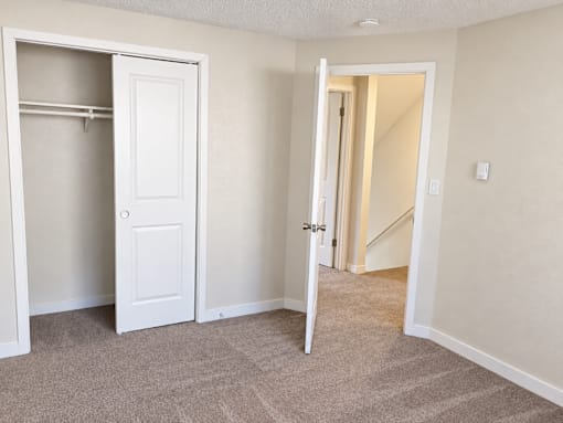 A room with two white doors, one open, and carpeted flooring.