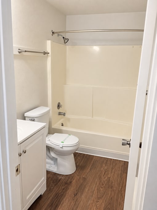 A white toilet with a white cabinet and a white bathtub in a bathroom.