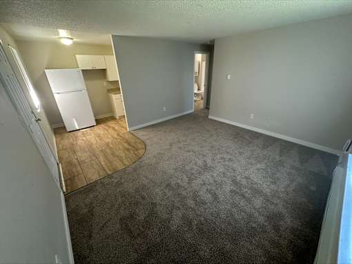 A room with a white fridge and a wooden floor.