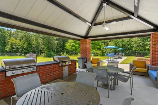 a covered patio with a barbecue and tables and chairs at The Madison of Tyler Apartment Homes, Tyler, Texas